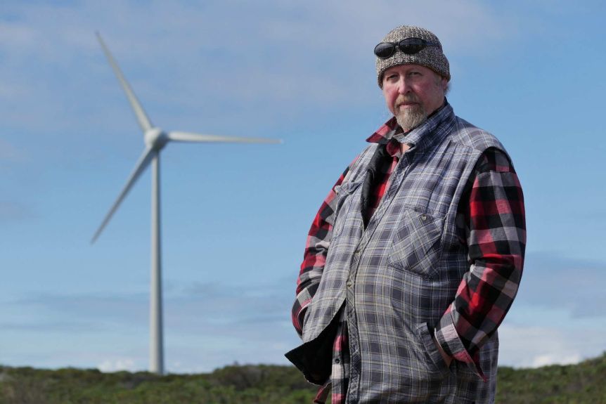 A man stands in front of a wind turbine